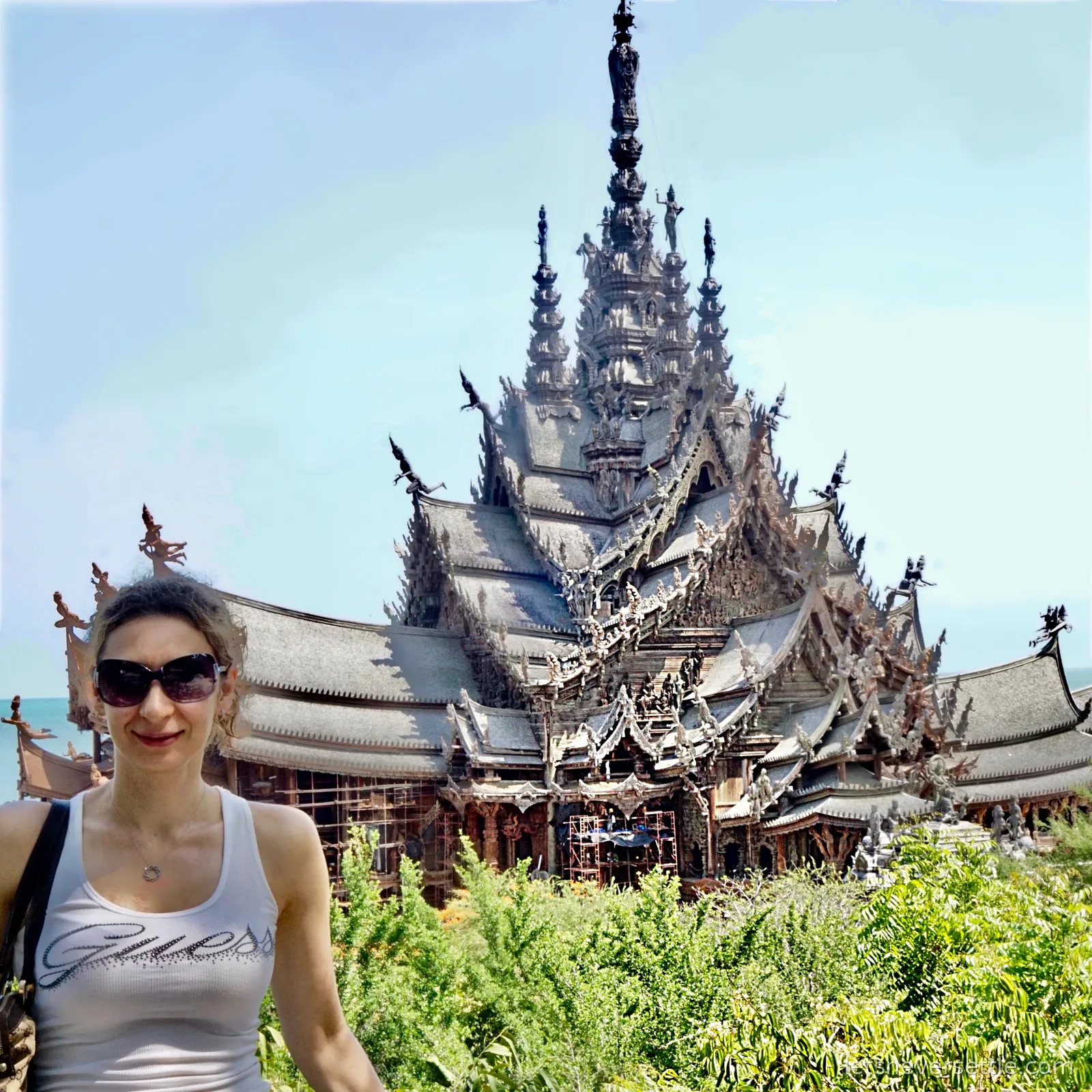 Inga in sunglasses standing in front of the Sanctuary of Truth, its many carved wooden spires rising behind her with the sea visible to the left