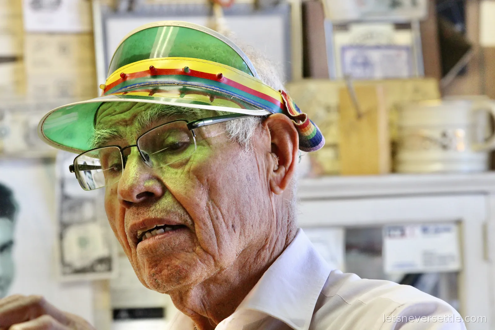 Angel Delgadillo in glasses and a colourful visor talking inside his gift shop, the walls covered in visitors' cards and dollar bills