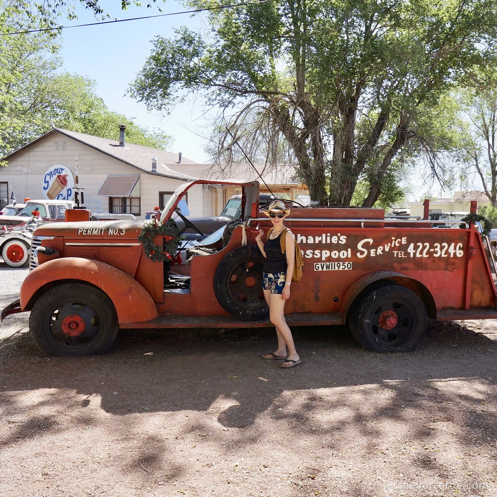 Inga in a straw hat posing beside a rusty vintage truck signwritten Charlie's Cesspool Service
