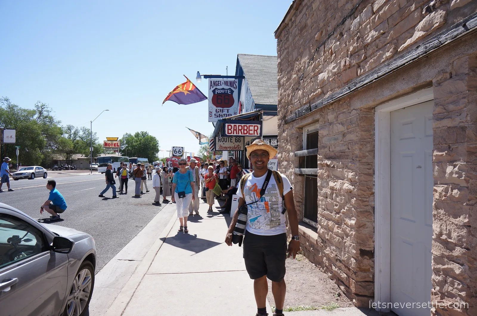 Dileep walking past a stone building towards barber shop and gift shop signs on Seligman's main street, with a tour group crossing the road