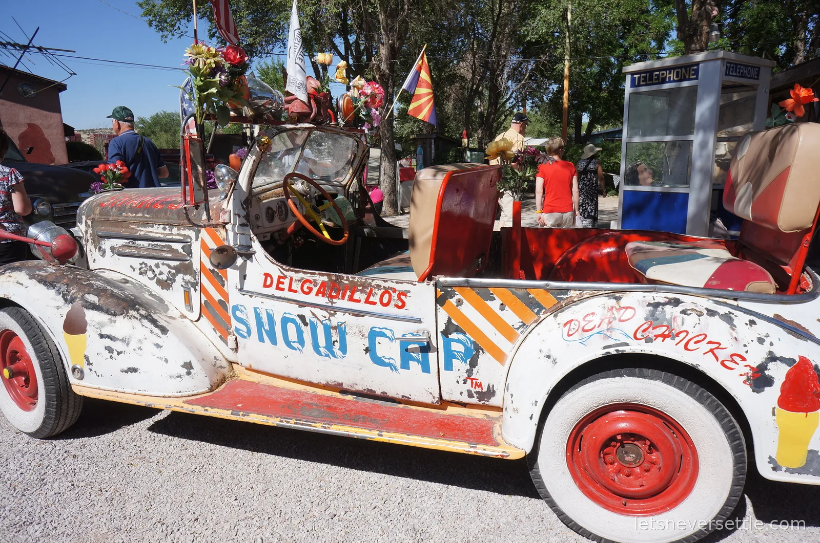 Delgadillo's Snow Cap vintage car painted white and red, decorated with flowers and flags, parked beside an old telephone box