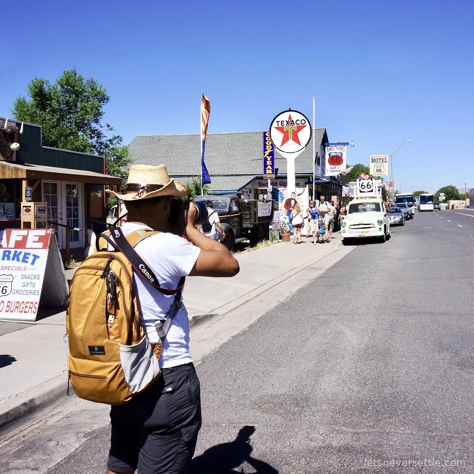 Dileep in a straw hat photographing the old Texaco sign and a line of Route 66 shopfronts from the roadside