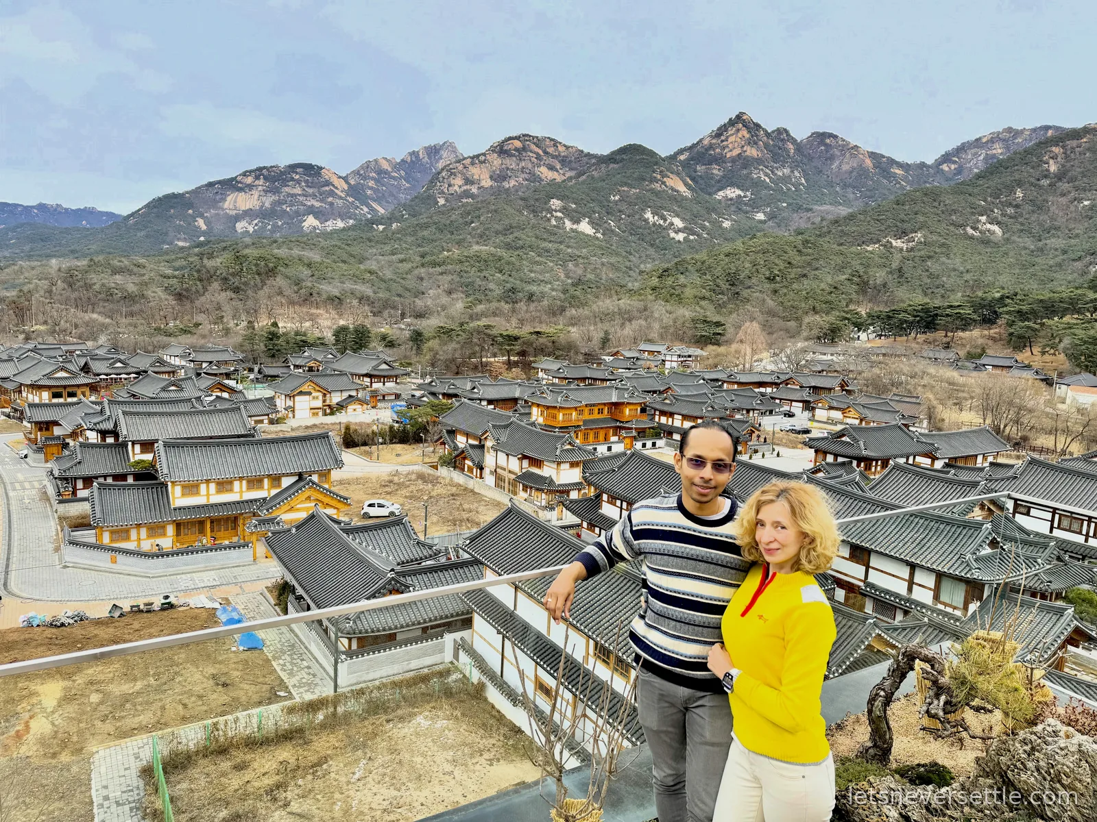 Inga and Dileep above the tiled rooftops of Eunpyeong Hanok Village, the granite peaks of Bukhansan behind