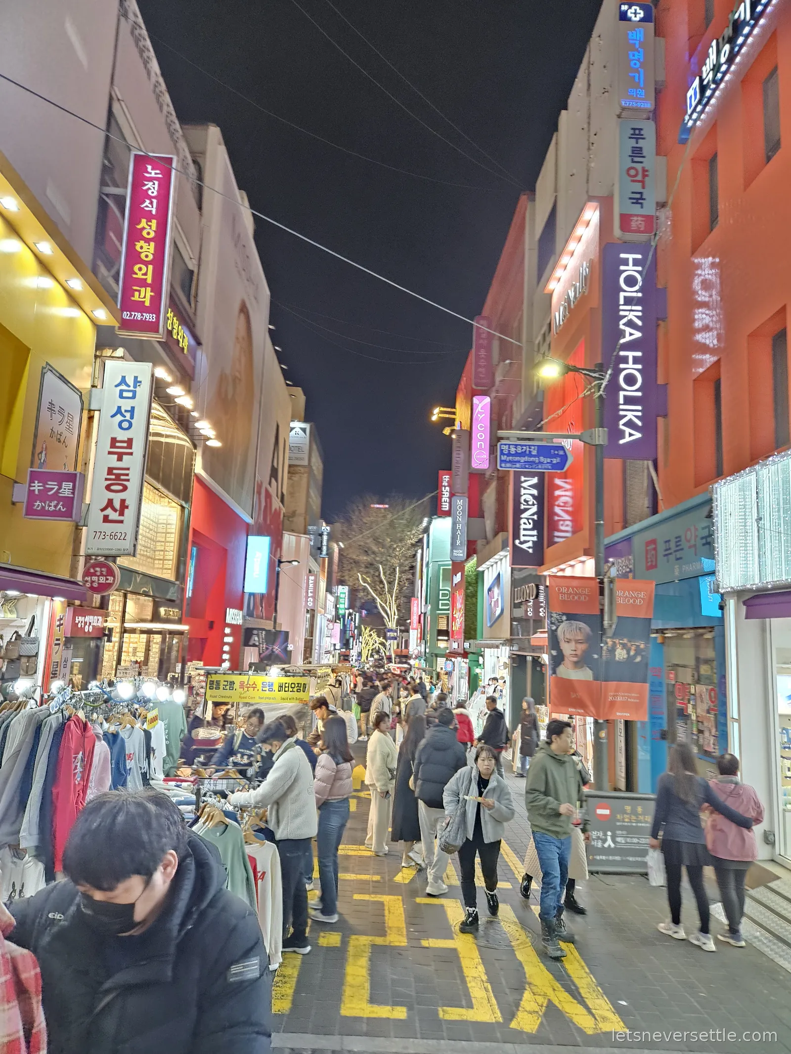 A busy Myeongdong street in Seoul late at night, lit shop signs in Korean stacked up the buildings and street food stalls still trading