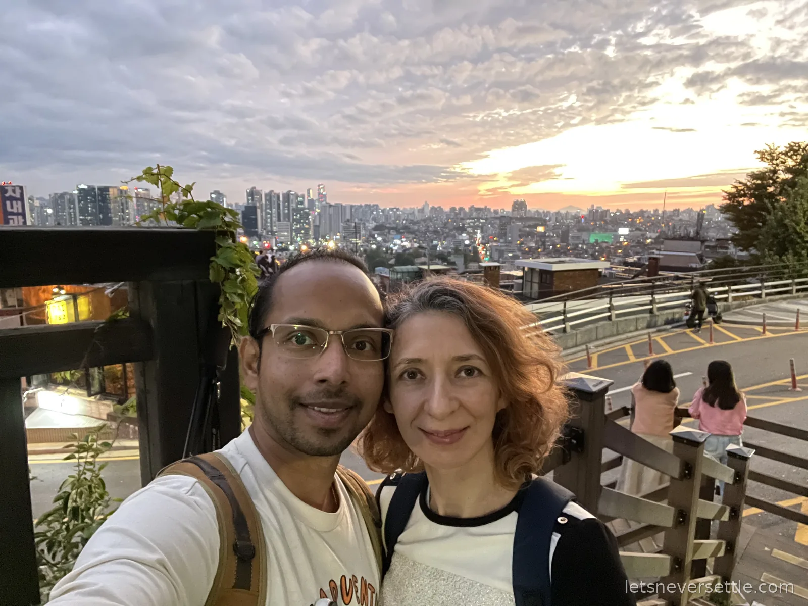 Selfie of Inga and Dileep on a terrace on Namsan's slopes, sunset glowing over the Seoul skyline behind them