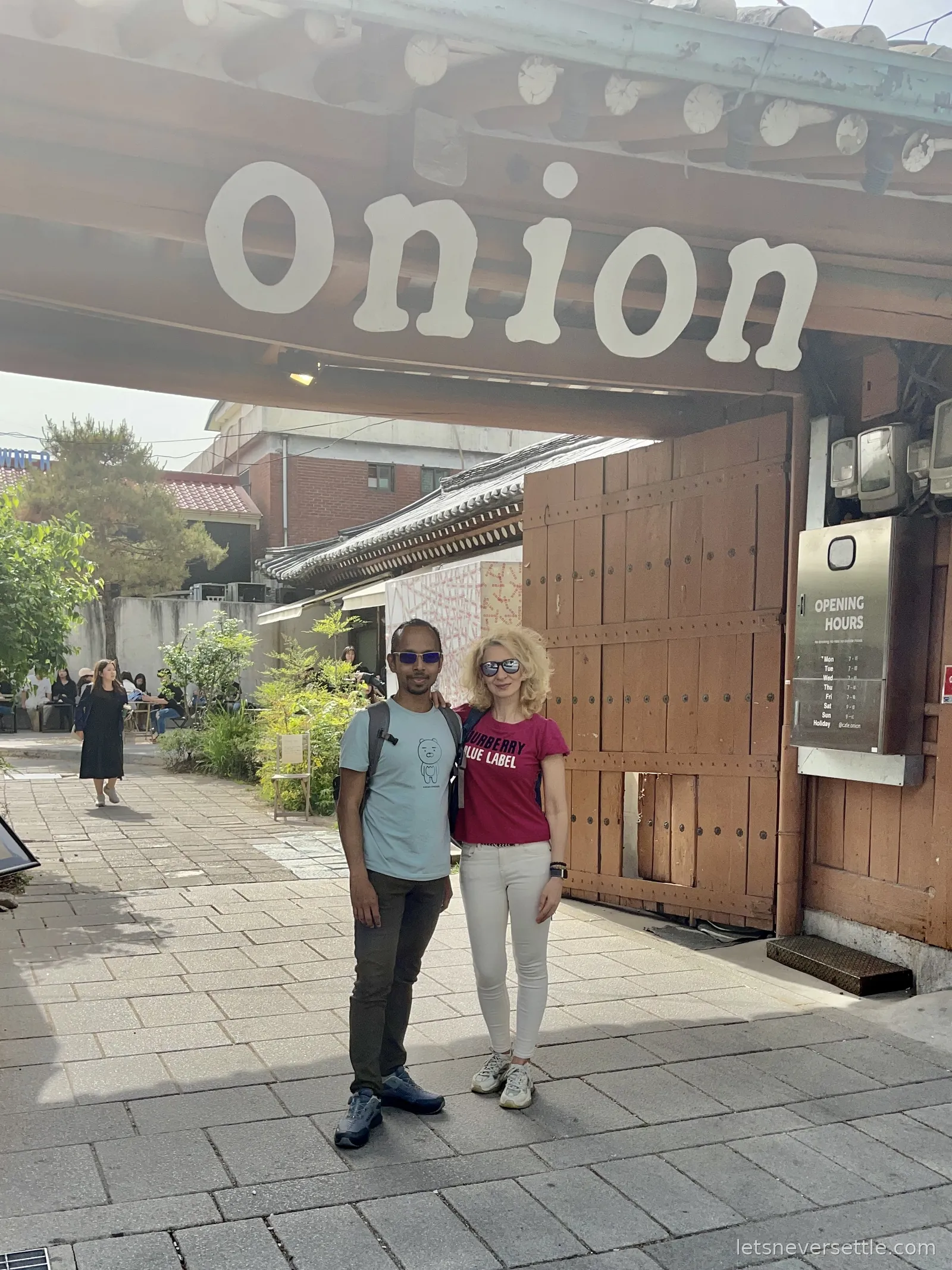 Inga and Dileep standing outside the Onion cafe in Anguk, Seoul, under a traditional wooden hanok gate with the Onion sign above it