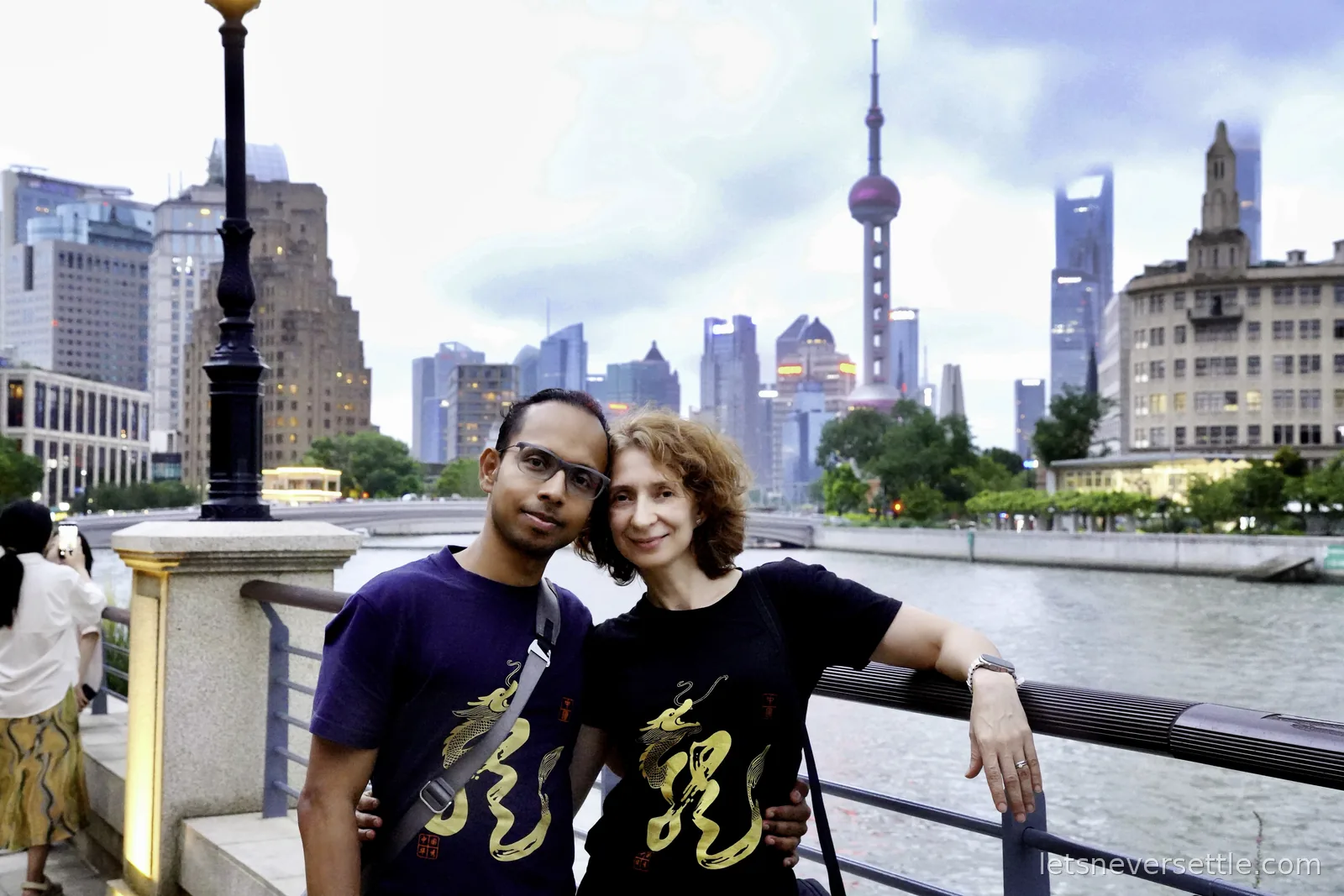 Inga and Dileep in matching golden dragon t-shirts on a Suzhou Creek bridge, the Oriental Pearl Tower and Pudong skyline behind