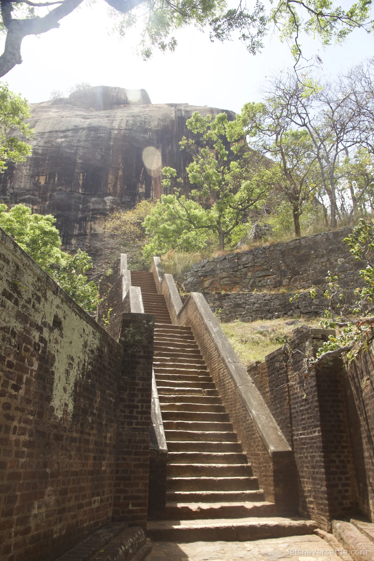 Steep brick staircase climbing between old walls and trees toward the rock face at Sigiriya