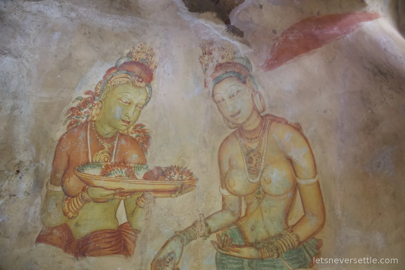 Two Sigiriya frescoes of crowned women, one holding a tray of flowers, painted on the sheltered rock face