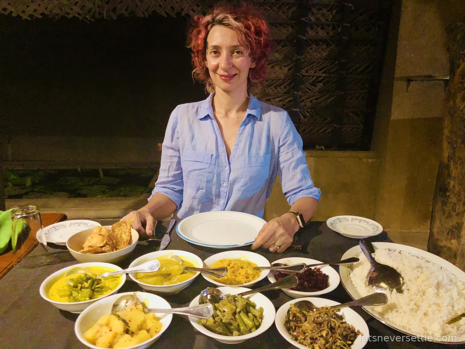 Inga at a table set with a Sri Lankan rice and curry spread: eight bowls of vegetable curries, sambols, poppadoms and a platter of rice
