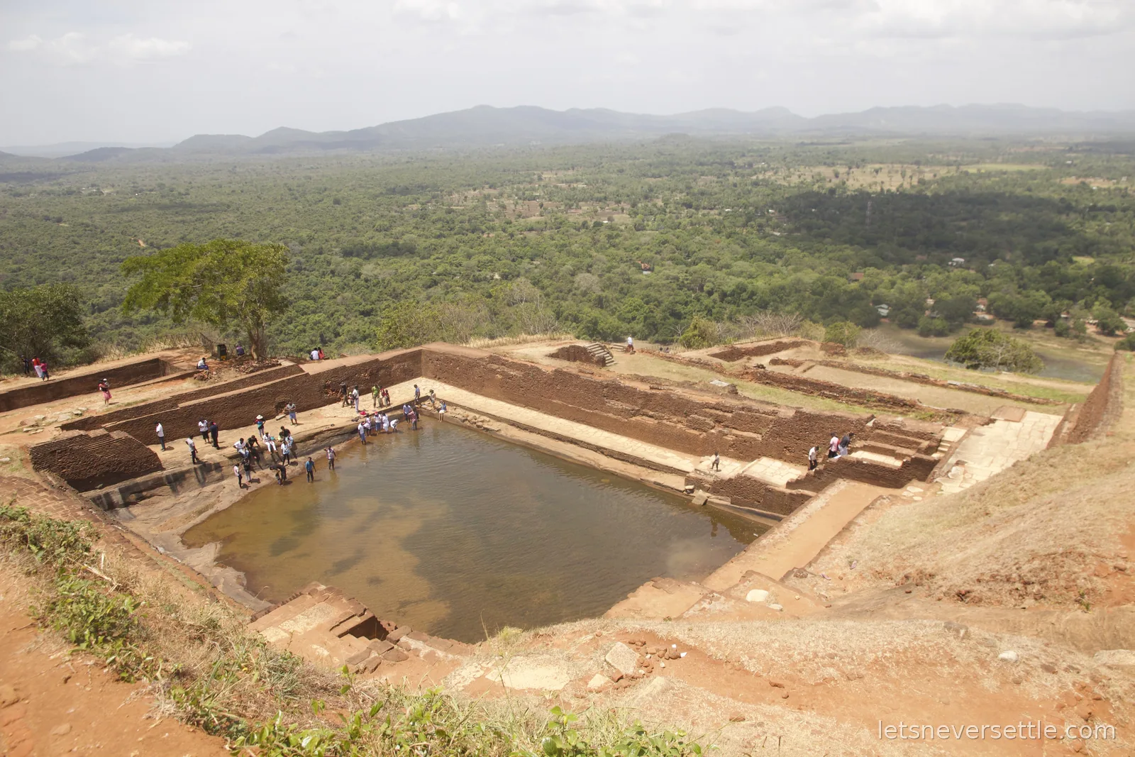 Large rock-cut water cistern on the summit of Sigiriya with visitors around it and green plains stretching below