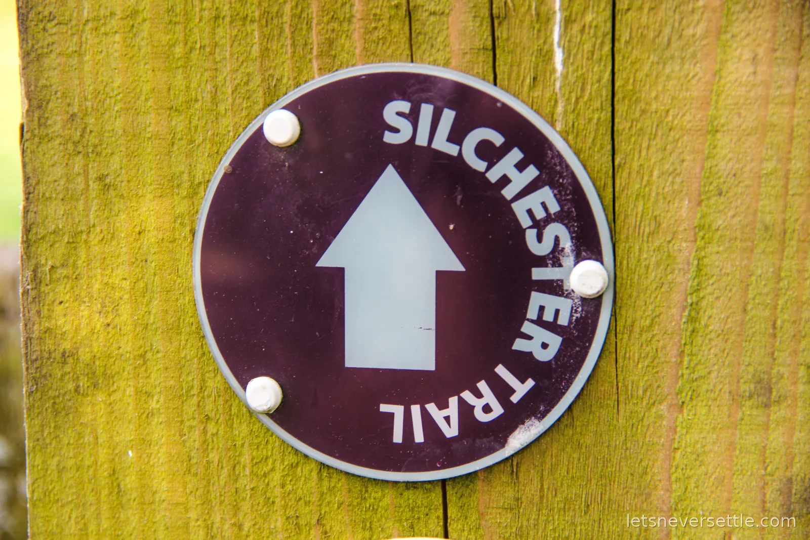 A round waymark disc on a wooden post reading Silchester Trail with a white arrow pointing straight on