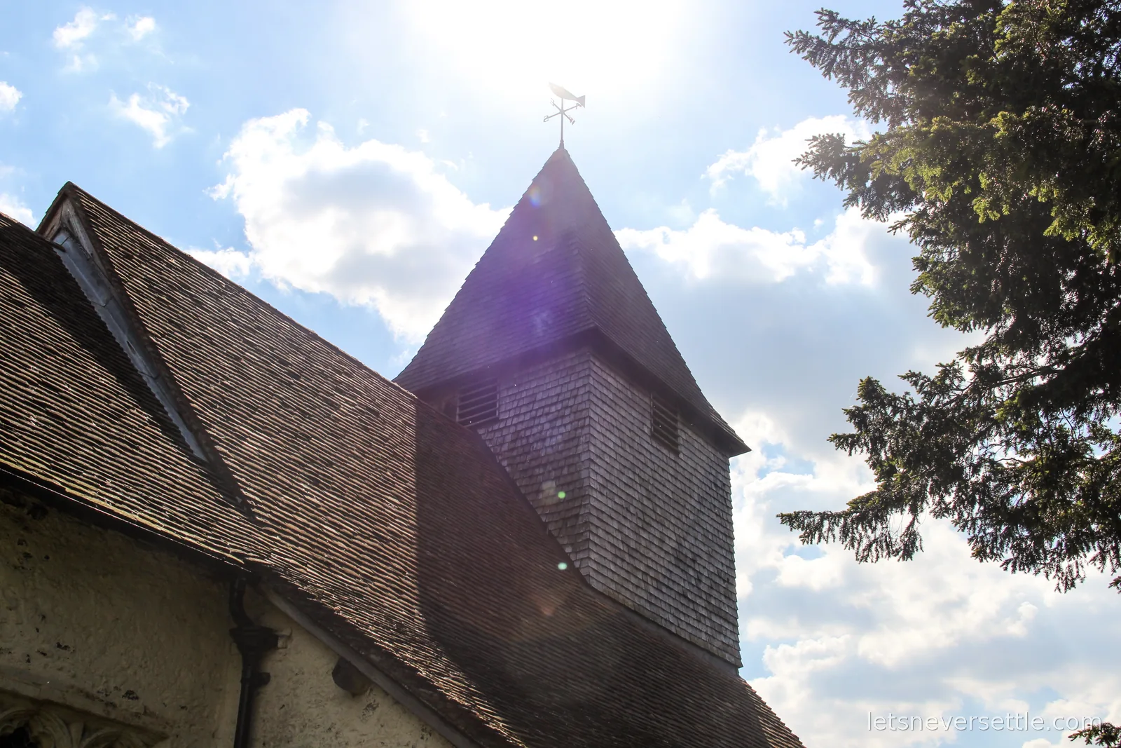 The wooden shingled tower and weathervane of St Mary's church at Silchester against the sun, the tiled church roof below