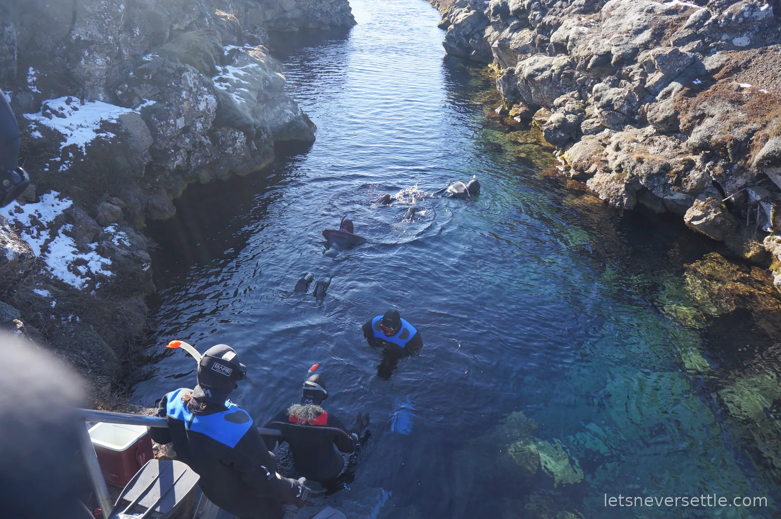 Looking down from the platform at a group of snorkellers entering the clear turquoise water of Silfra between rock walls