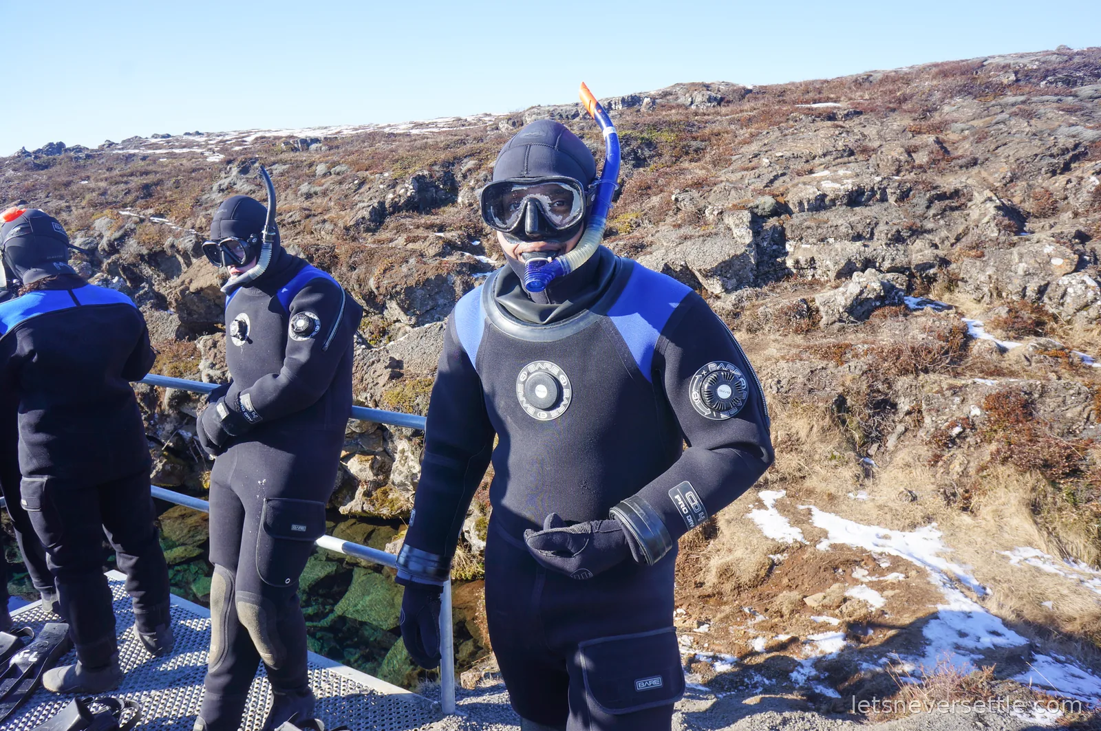 Dileep in a hood, mask and snorkel standing on the metal entry platform at Silfra while other snorkellers wait behind him