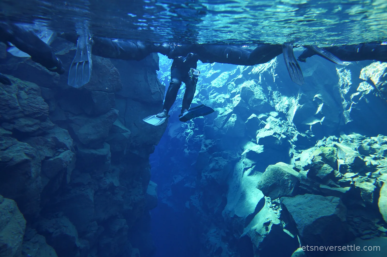 Line of snorkellers floating along the mirrored surface of the water at Silfra, seen from below between two rock walls