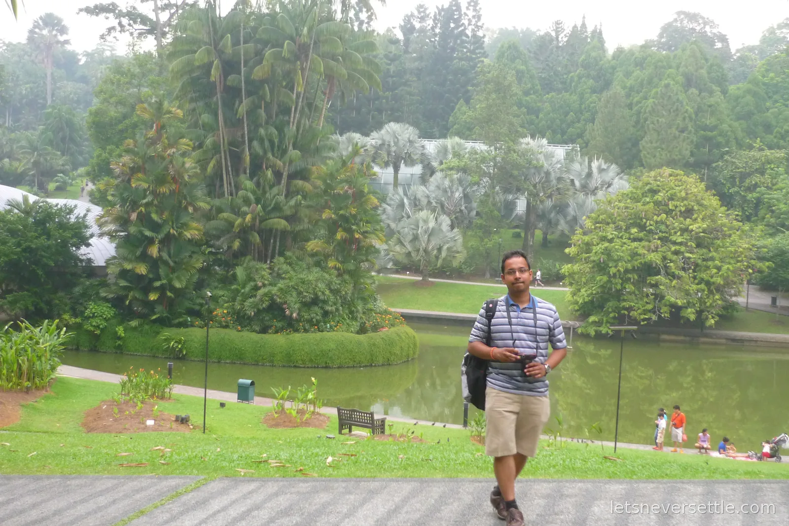 Dileep with a camera in the Singapore Botanic Gardens, palms and a lake in the background