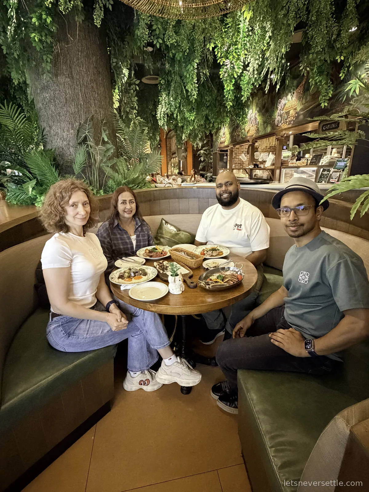 Four of us around a table of plates in a curved booth beneath a canopy of hanging greenery at a VivoCity restaurant
