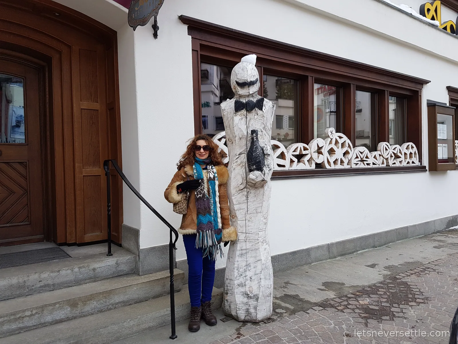 Inga standing beside a life sized carved white wooden figure of a waiter in a bow tie holding a bottle, next to a restaurant door