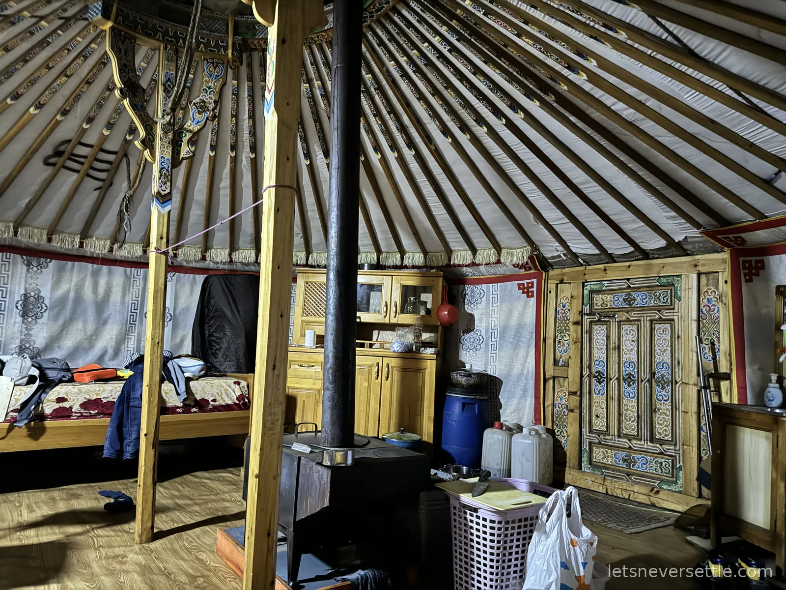 Inside a Mongolian ger: painted orange roof poles radiating from the crown, a central stove and chimney, cupboards and an ornately painted door