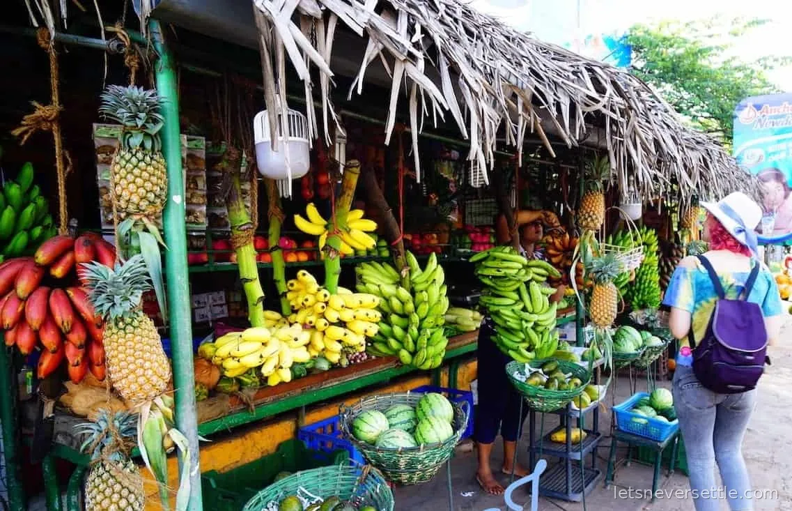 A vendor reading a newspaper at a roadside banana stall in Sri Lanka surrounded by hanging bunches