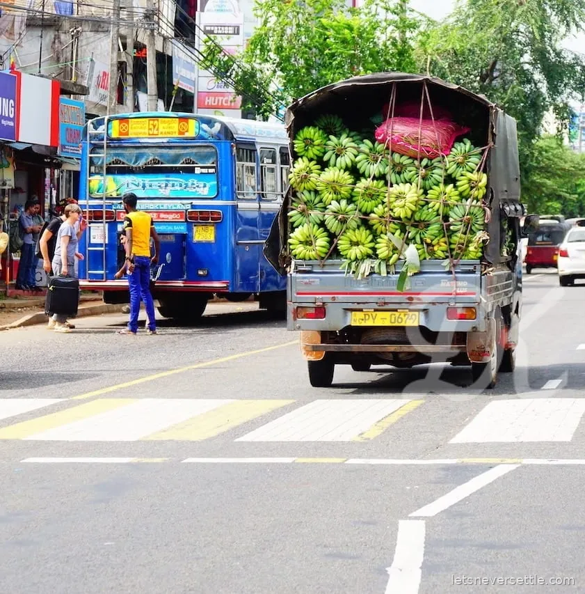 A small truck on a Sri Lankan road loaded above the cab height with green banana bunches