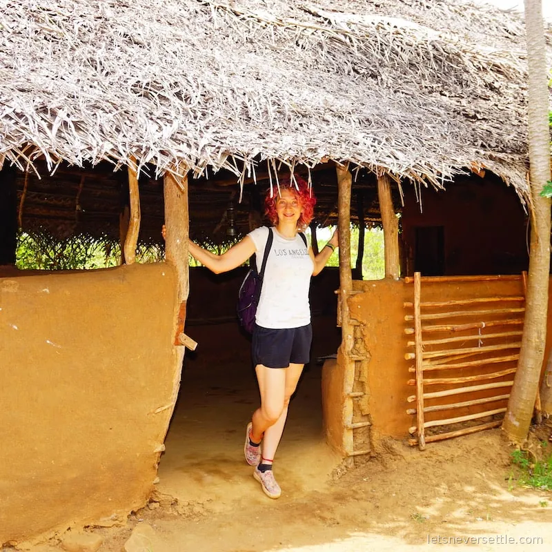 Inga standing in the doorway of a traditional mud hut with a thatched roof in Sri Lanka