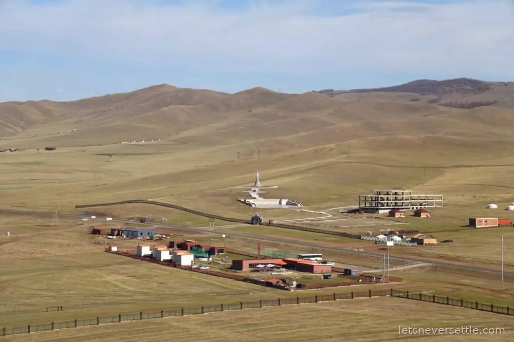 A small cluster of white gers and animal pens on the open Mongolian plain seen from a low hill