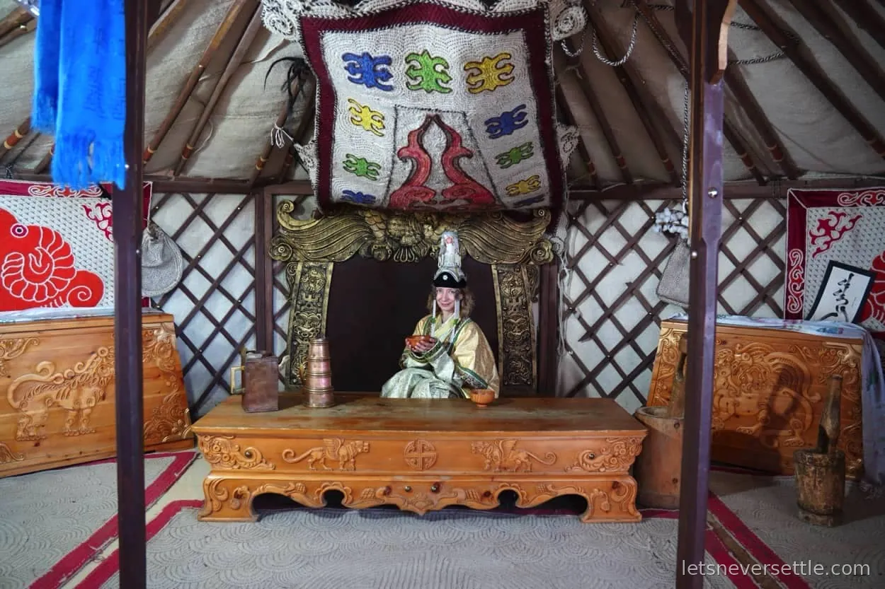 The painted wooden interior of a Mongolian ger with an orange lattice frame, patterned quilts and a low bed