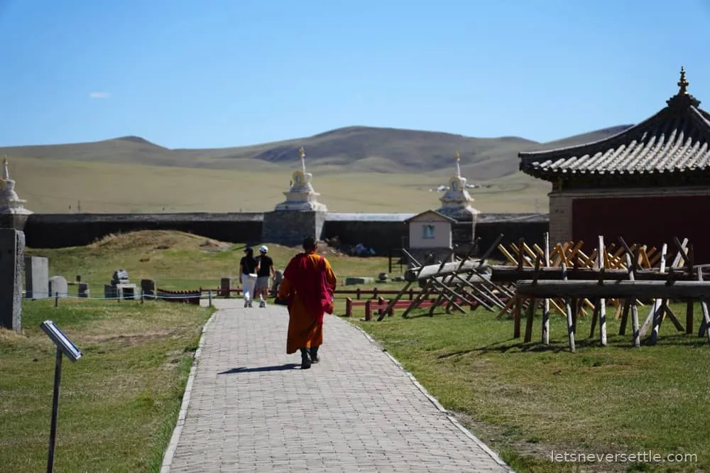 A monk in red robes walking along a paved path between temple buildings at Erdene Zuu monastery