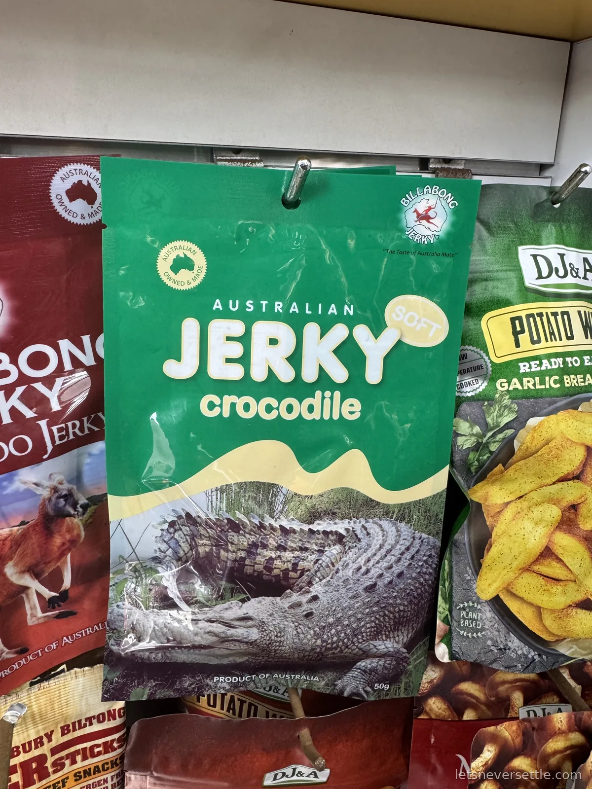 A green packet of Australian crocodile jerky hanging on a shop shelf between kangaroo jerky and potato wedges