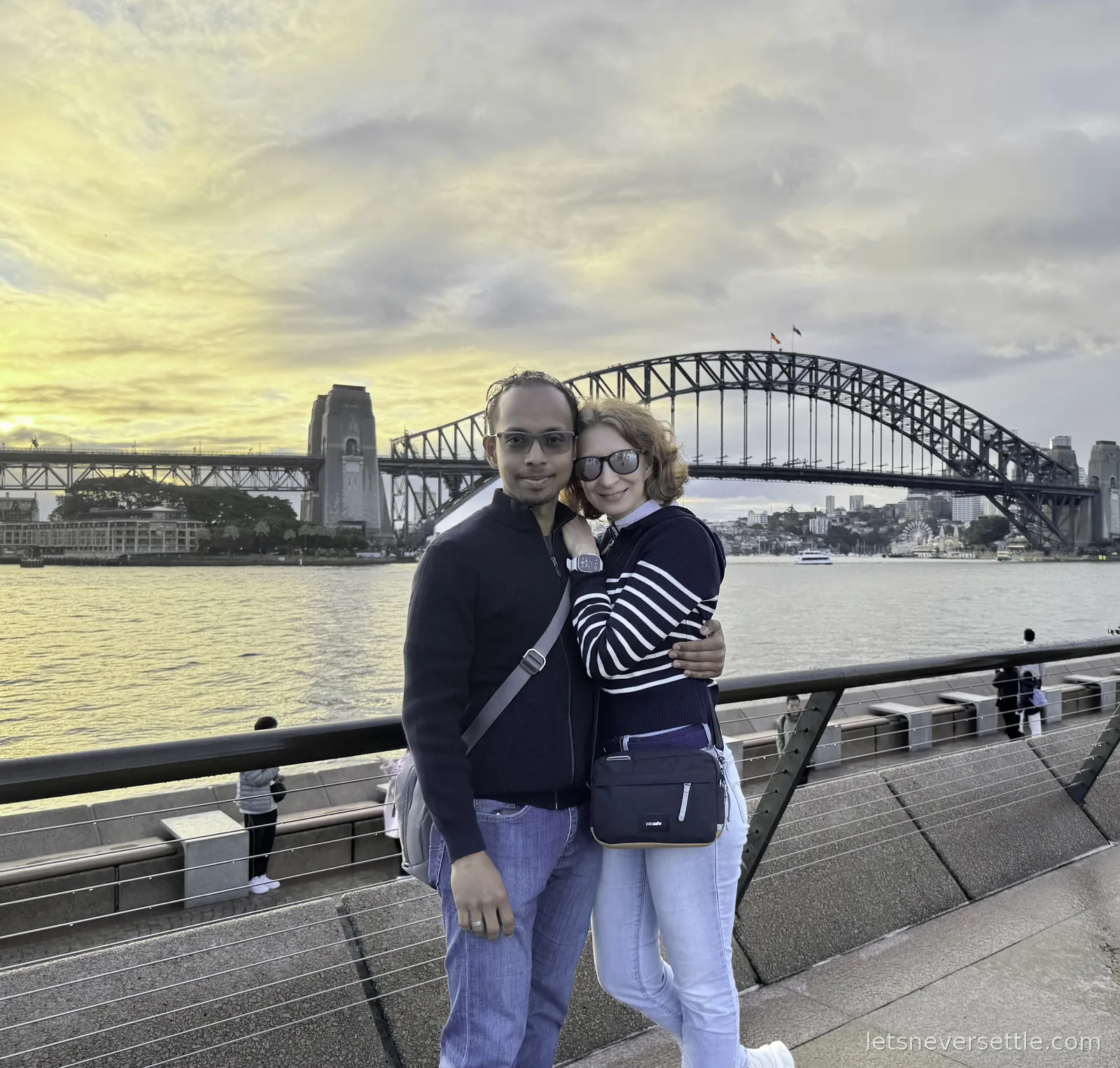 Inga and Dileep in front of Sydney Harbour Bridge at sunset, yellow sky behind the steel arch
