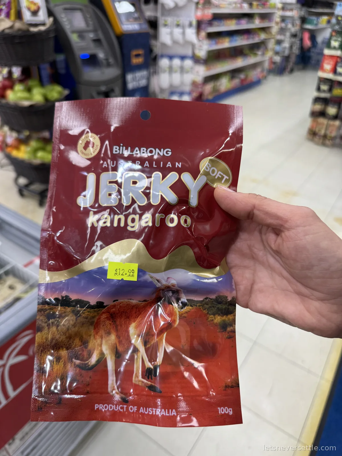 A hand holding a red packet of Billabong Australian kangaroo jerky priced at 12.99 dollars in a shop