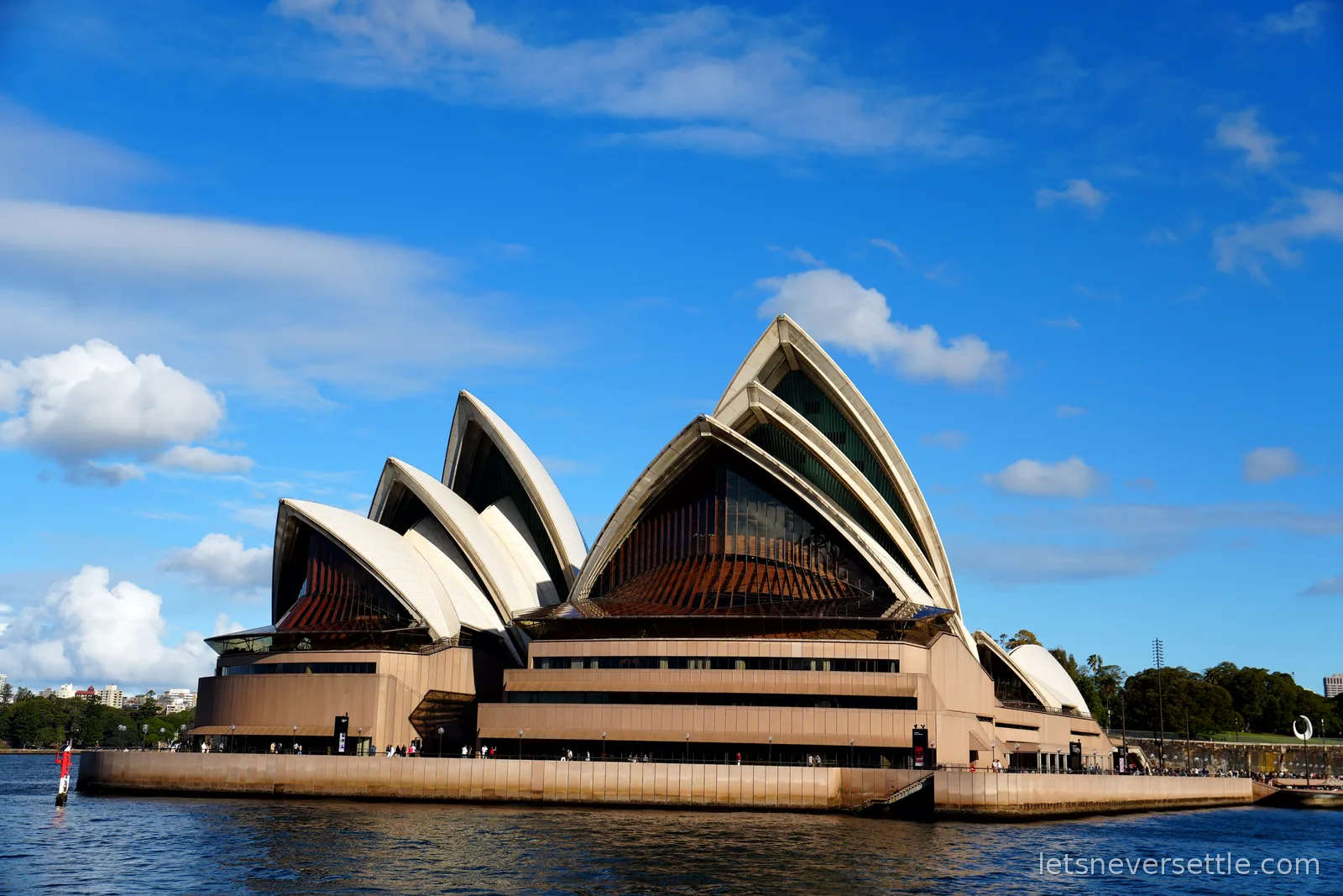 Sydney Opera House seen side-on from the harbour under a bright blue sky with scattered clouds