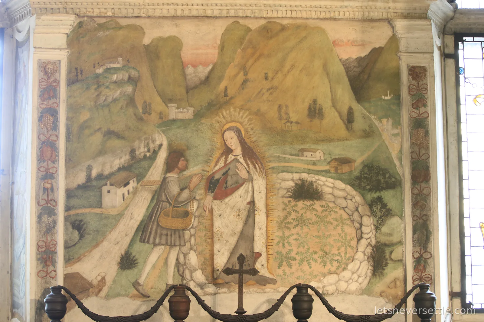A faded wall fresco of the same scene, a haloed woman meeting a man carrying a basket on a path winding between green hills and small farmhouses