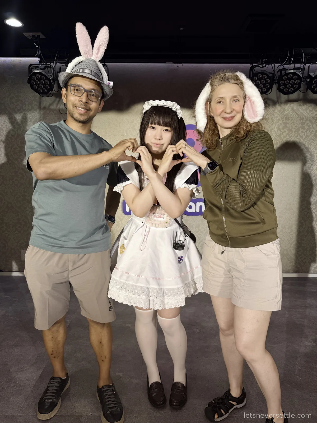 Dileep and Inga standing either side of a maid in a white uniform, all three making heart shapes with their hands
