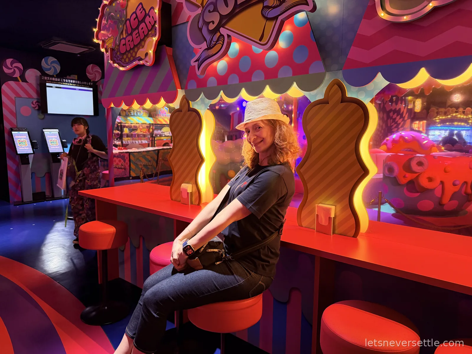 Inga in a straw hat sitting on a red stool at a candy-coloured counter under a neon ice cream sign inside Monster Girls in Harajuku