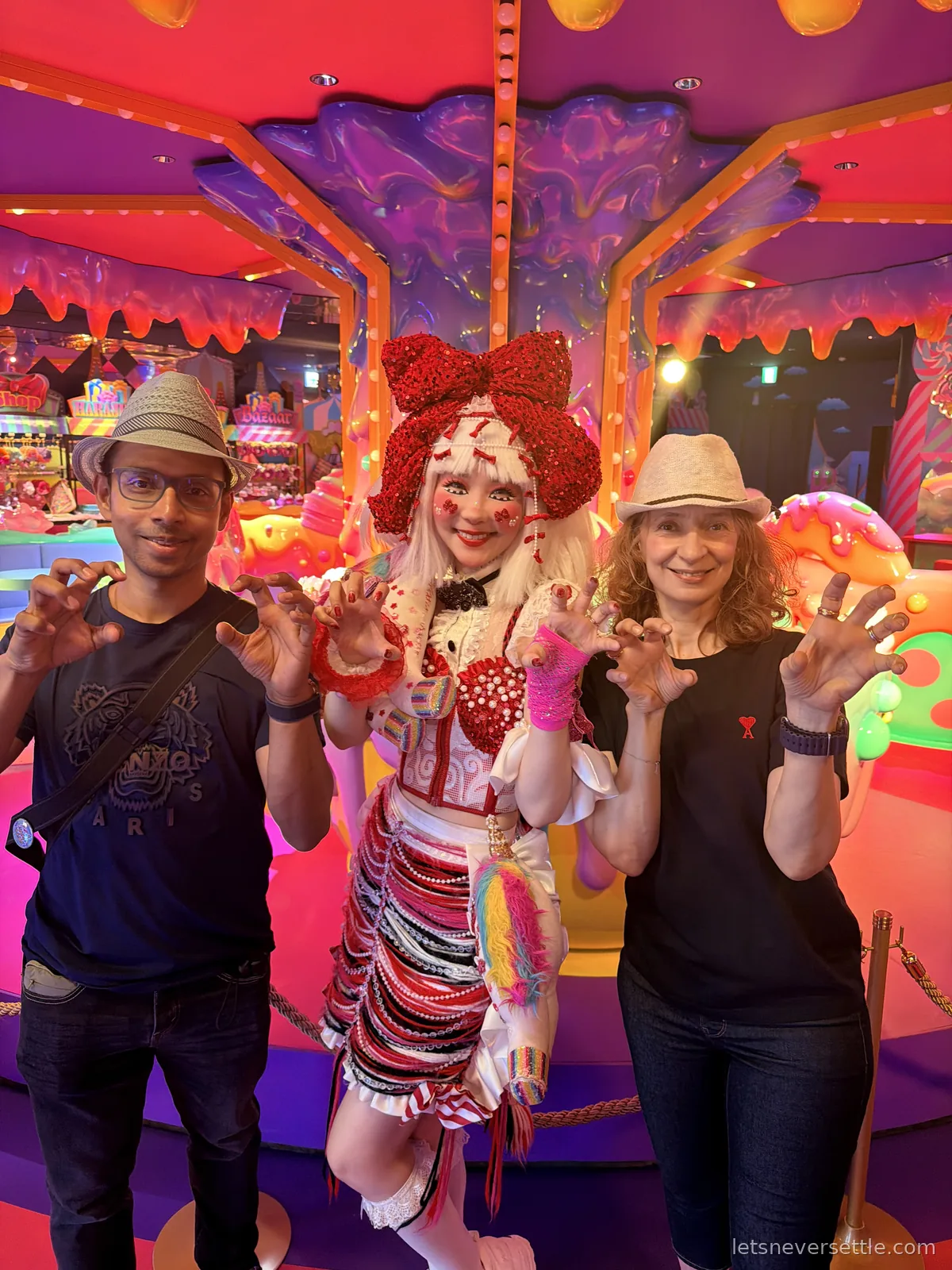 Dileep and Inga in straw hats making claw hands either side of a performer wearing a giant red bow and a striped skirt