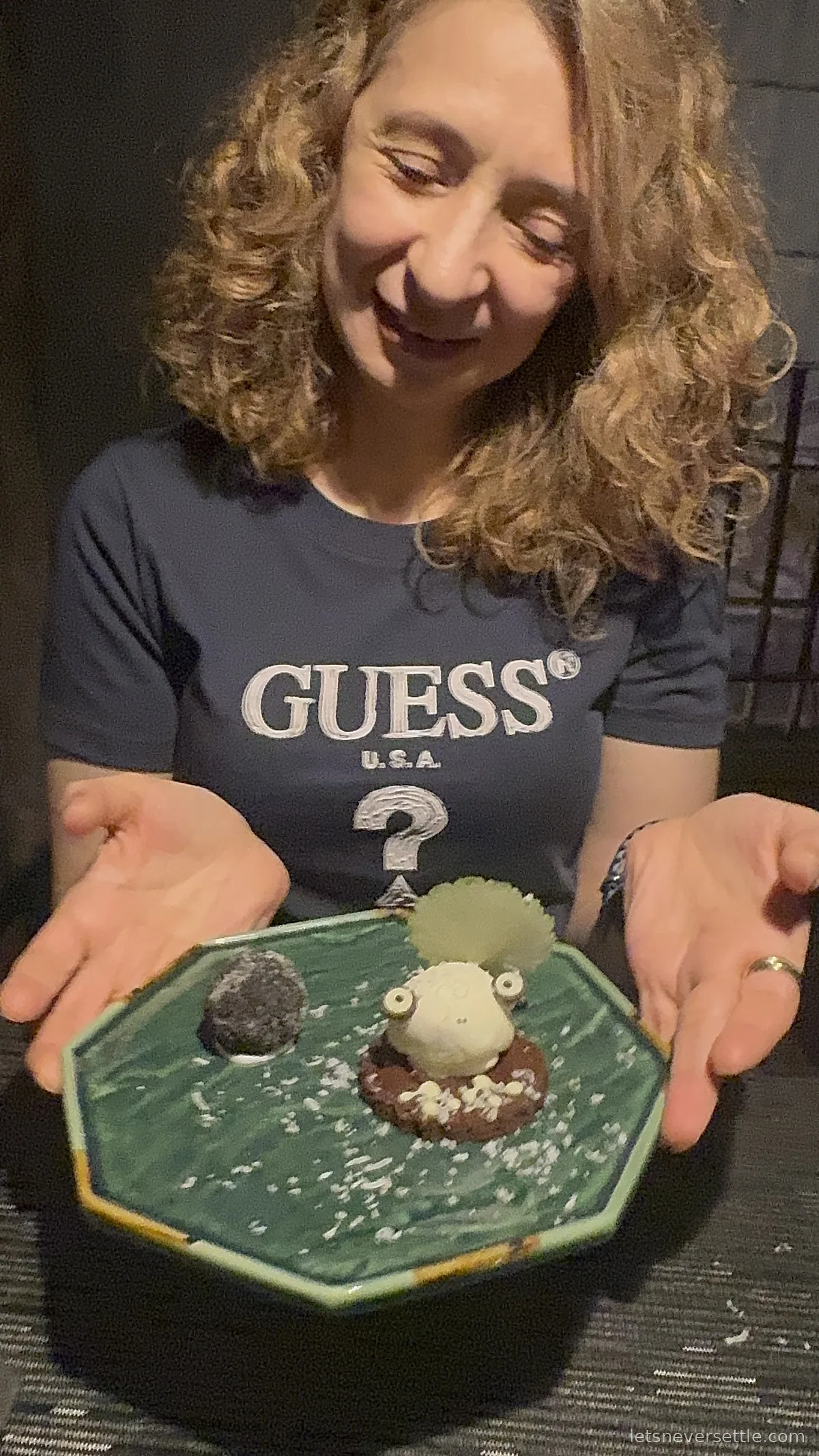 Inga holding an octagonal green dessert plate with a small white sugar creature sitting on a chocolate disc, dusted with coconut