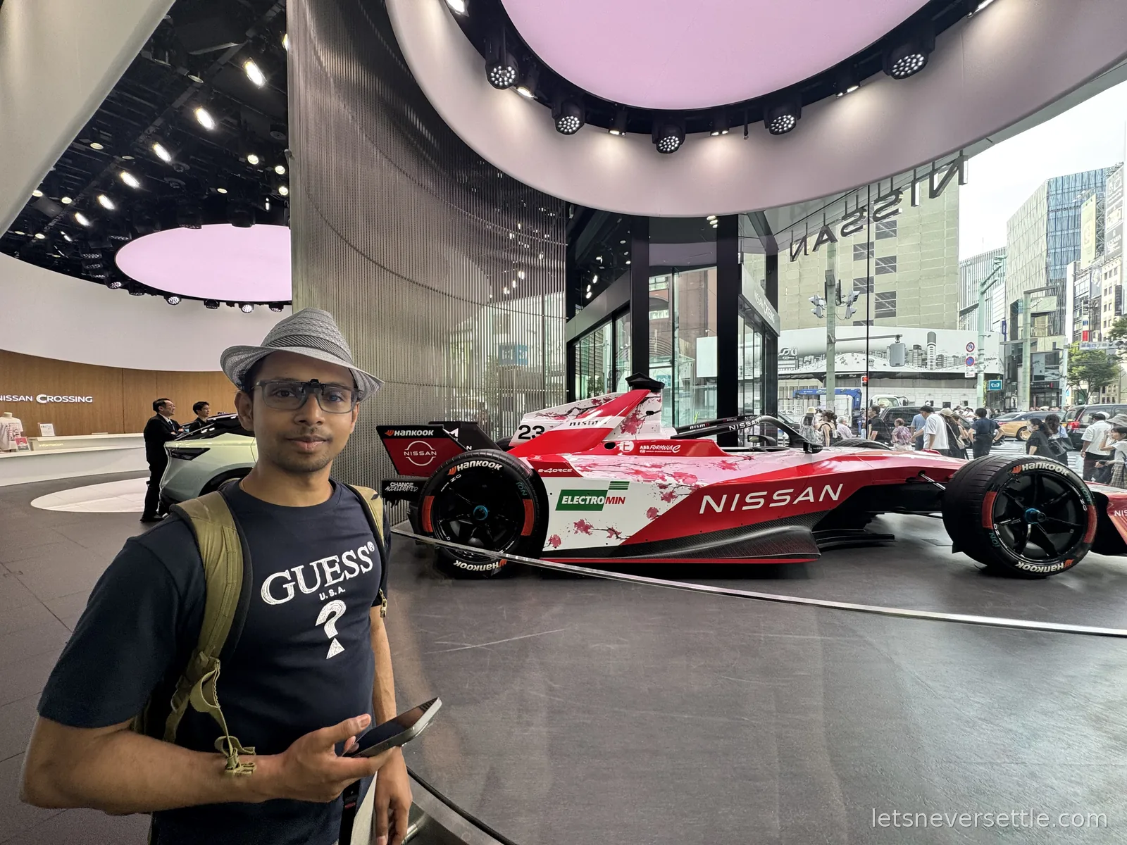Dileep standing in front of a red and white number 23 Nissan Formula E car in cherry blossom livery inside the Nissan Crossing showroom in Ginza