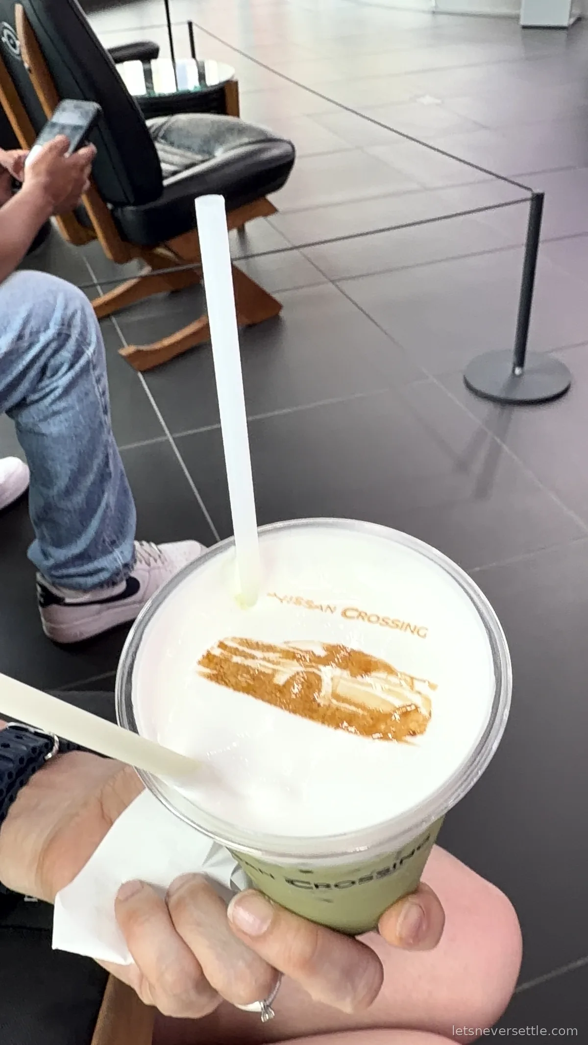A hand holding a paper cup of latte with a car and the words Nissan Crossing printed in the milk foam