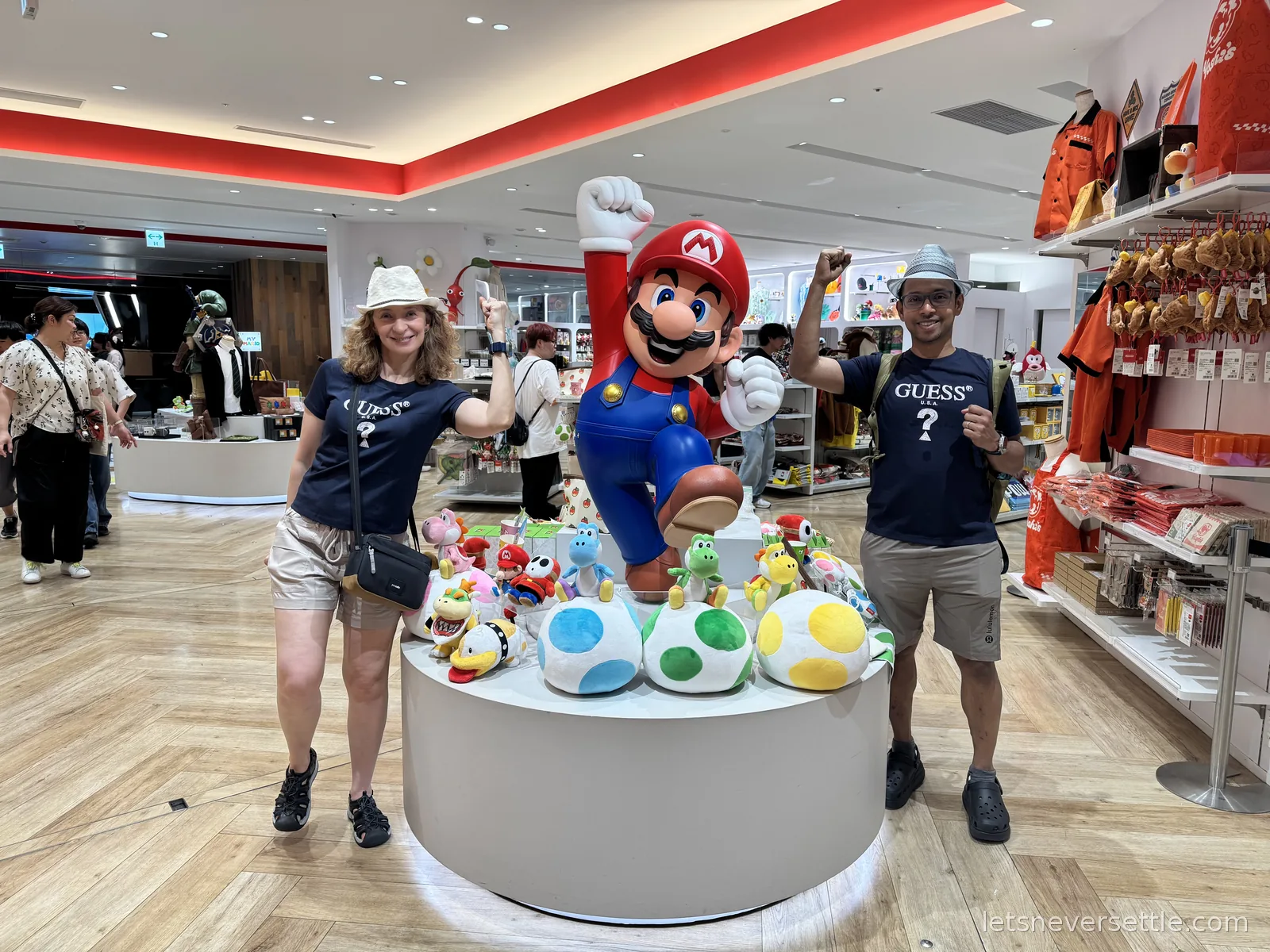 Inga and Dileep posing on either side of a Mario statue surrounded by Yoshi egg plushies in the Nintendo Tokyo store