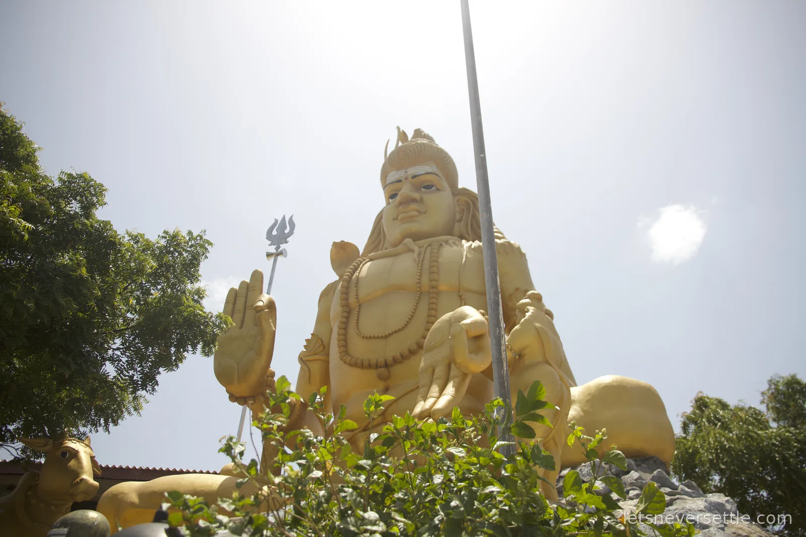 A towering golden statue of Shiva with a trident, seen from below against a bright sky at Koneswaram temple
