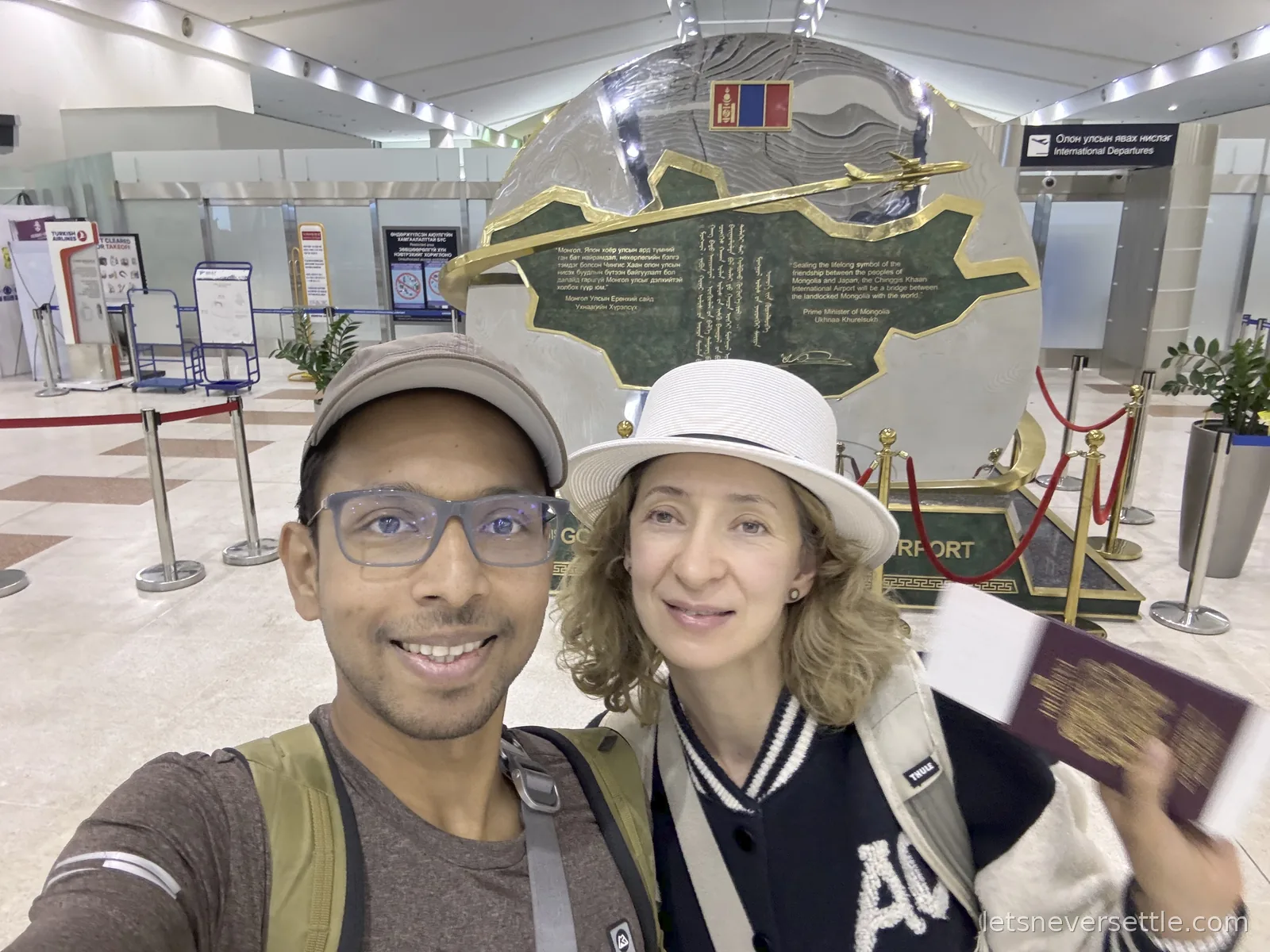 Selfie of Dileep and Inga with passports at the Chinggis Khaan International Airport friendship monument in the terminal