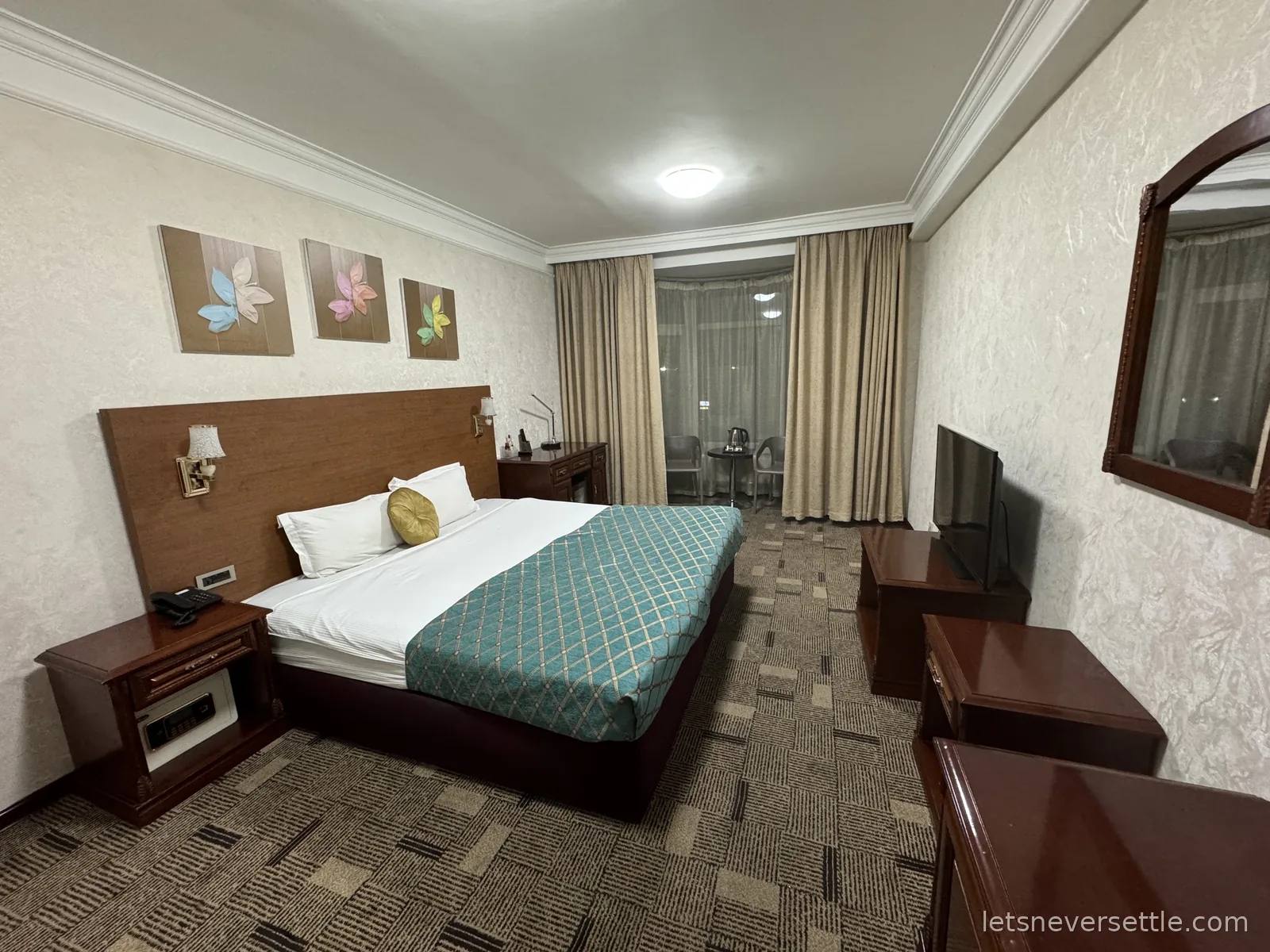 Ulaanbaatar hotel room with a large bed under a teal quilted runner, wood furniture and a kettle set by the bay window