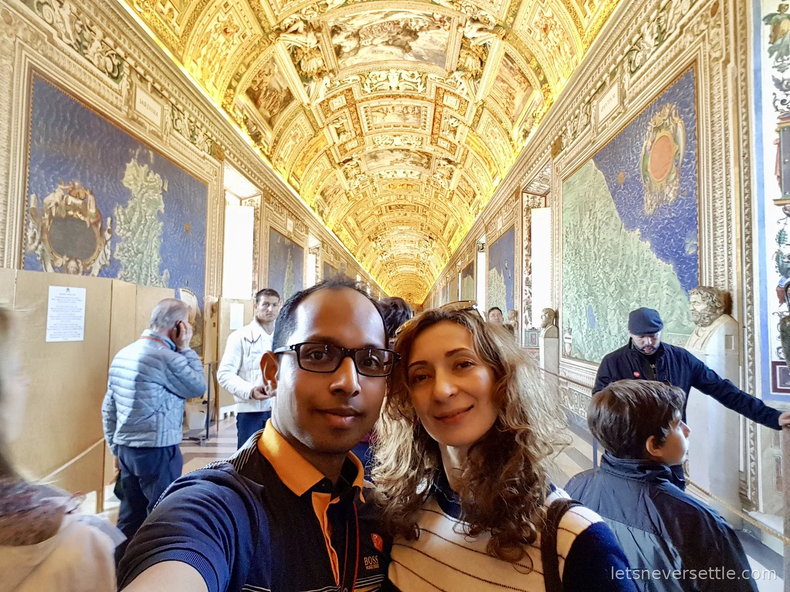 Inga and Dileep taking a selfie in the Gallery of Maps with the gilded vault and blue map panels stretching away behind them