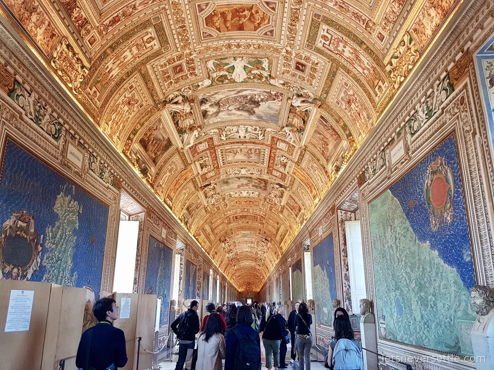The Gallery of Maps, a long corridor with a heavily gilded painted vault and huge painted maps on blue backgrounds down both walls, filled with visitors