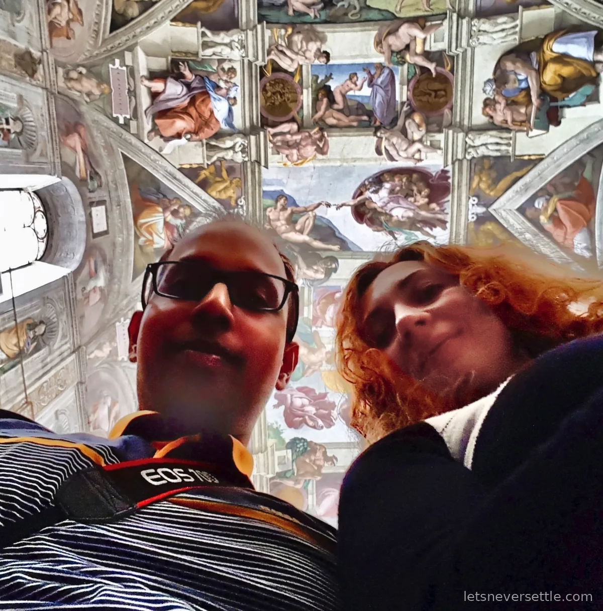 Inga and Dileep looking up at the Sistine Chapel ceiling, with the Creation of Adam visible directly above them