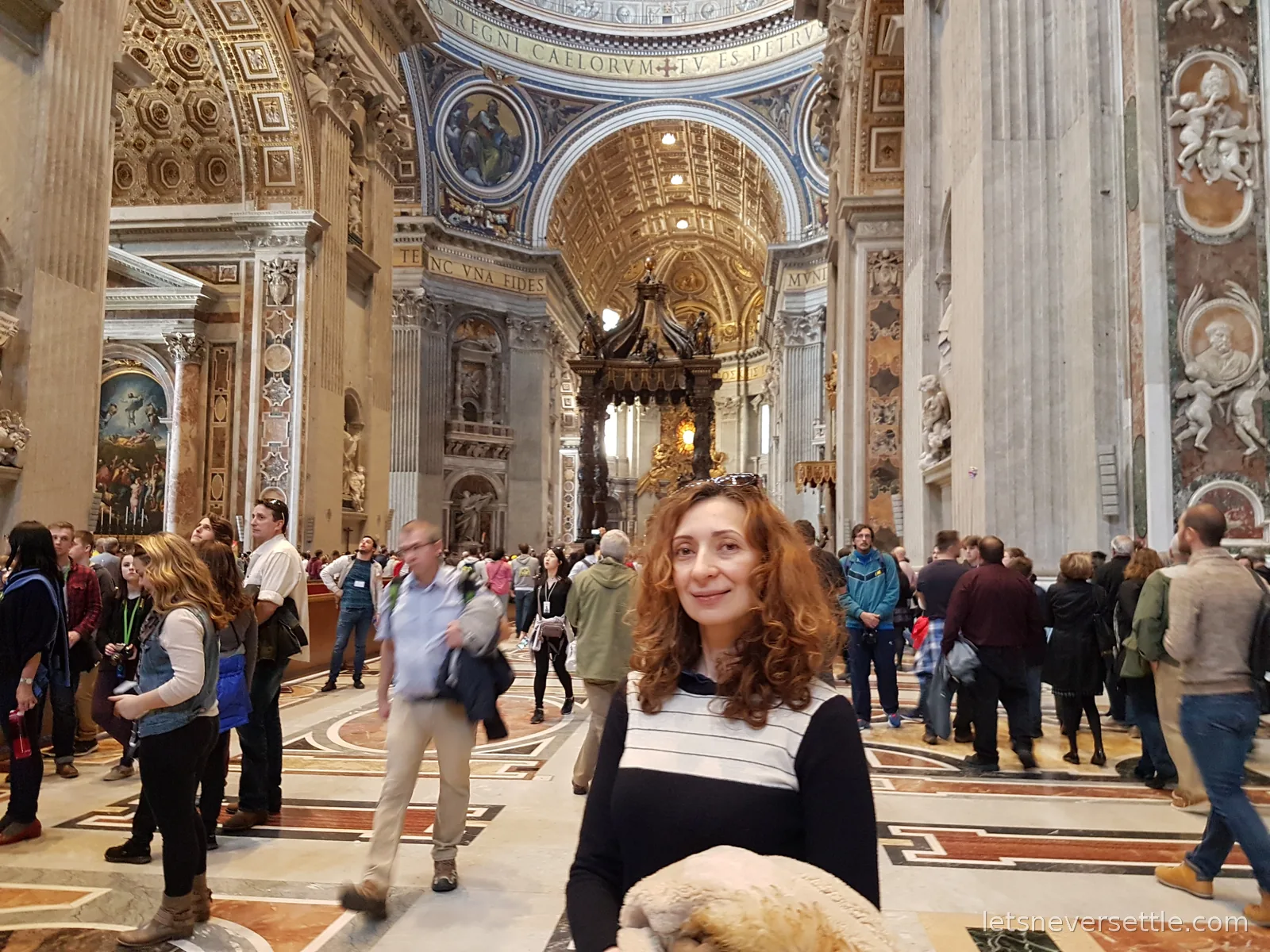 Inga smiling in the nave of St Peter's Basilica with the bronze baldachin under the dome behind her and crowds on the marble floor