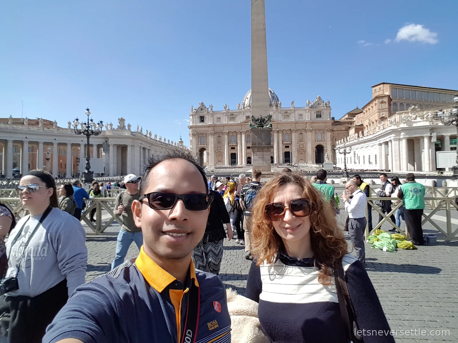 Inga and Dileep taking a selfie in St Peter's Square with the obelisk, the basilica front and the colonnade behind them